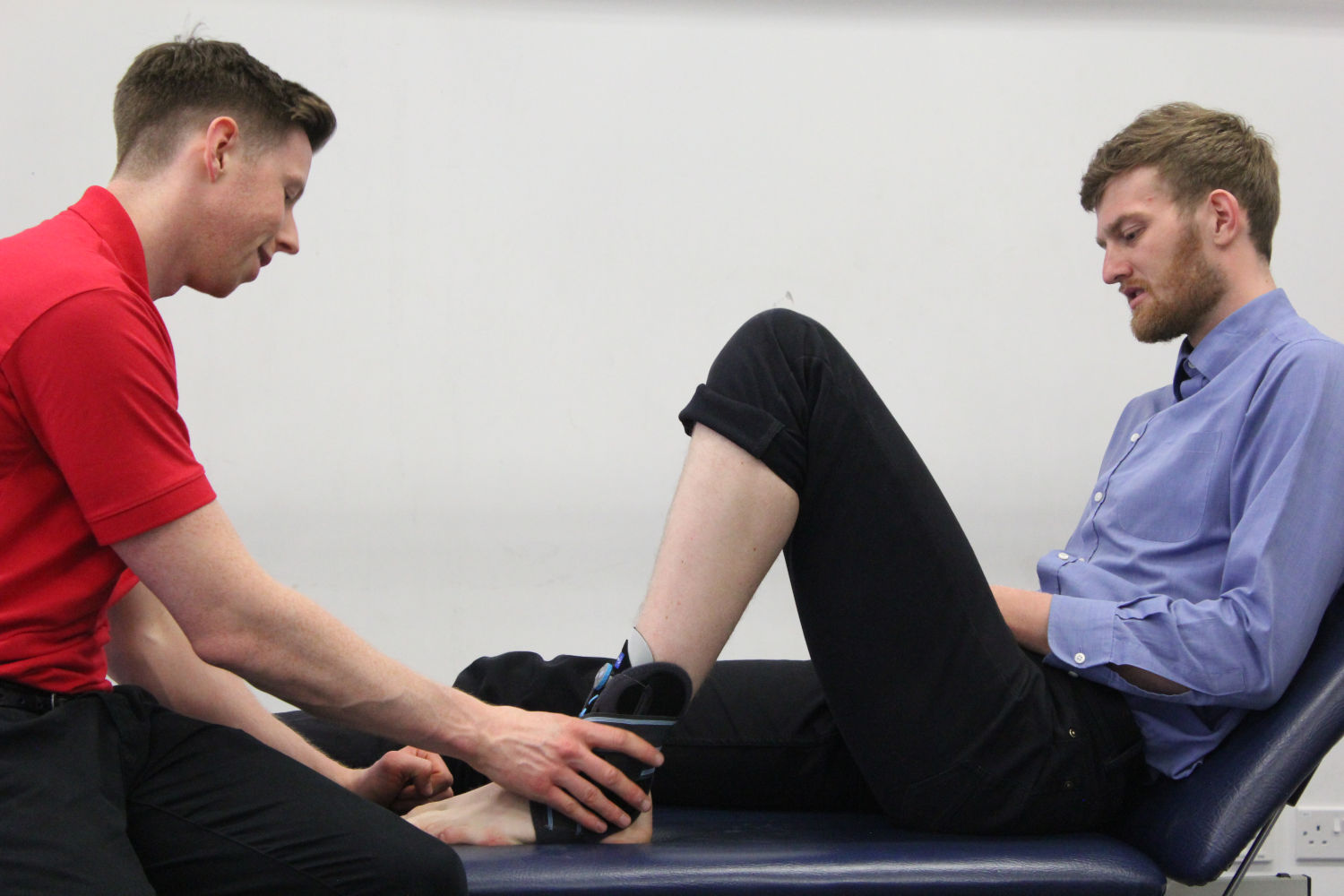 Man sat on table wearing ankle support.